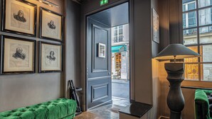 A hallway with framed portraits, a green sofa, a lamp, and a door leading outside. - Hotel Saint-Louis en L'Isle - Notre-Dame (Paris)