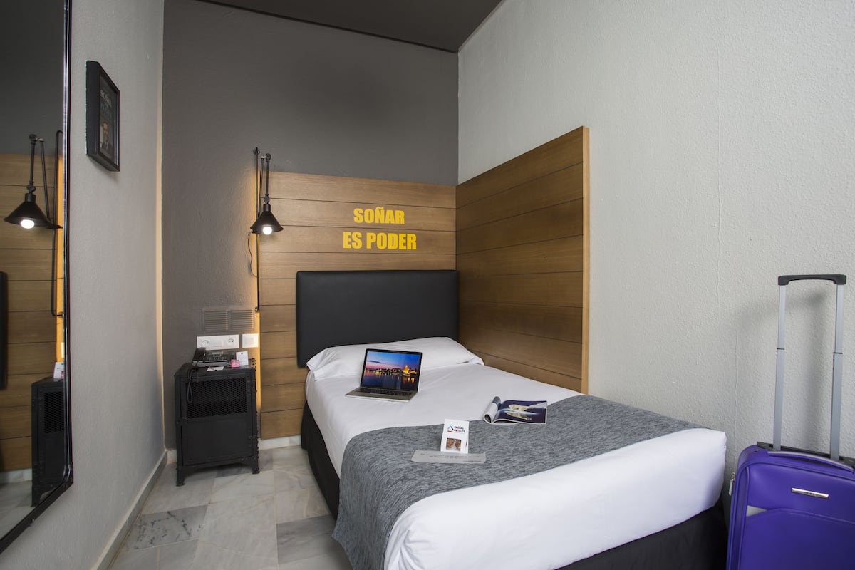 Una habitación de hotel moderna con una cama, un escritorio con una computadora portátil, una maleta y una cita motivacional en la pared.