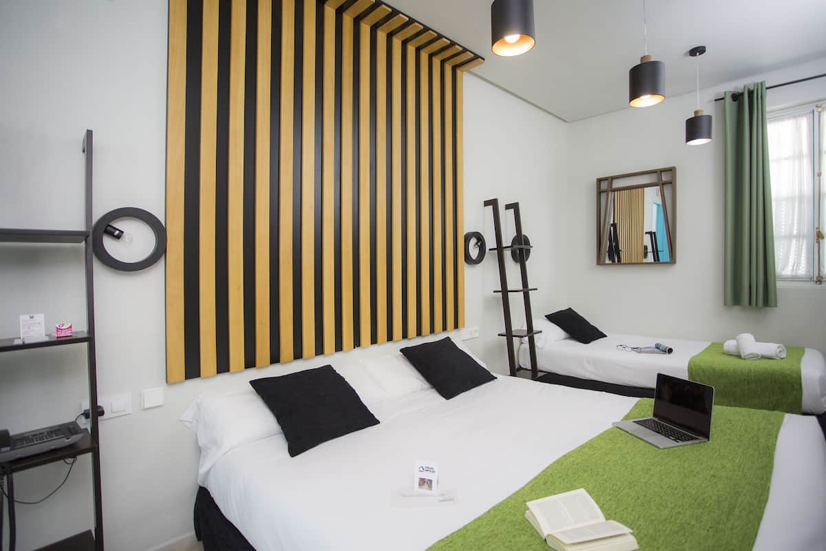 Habitación de hotel con dos camas, un escritorio con una computadora portátil, un espejo y un diseño de pared a rayas.
