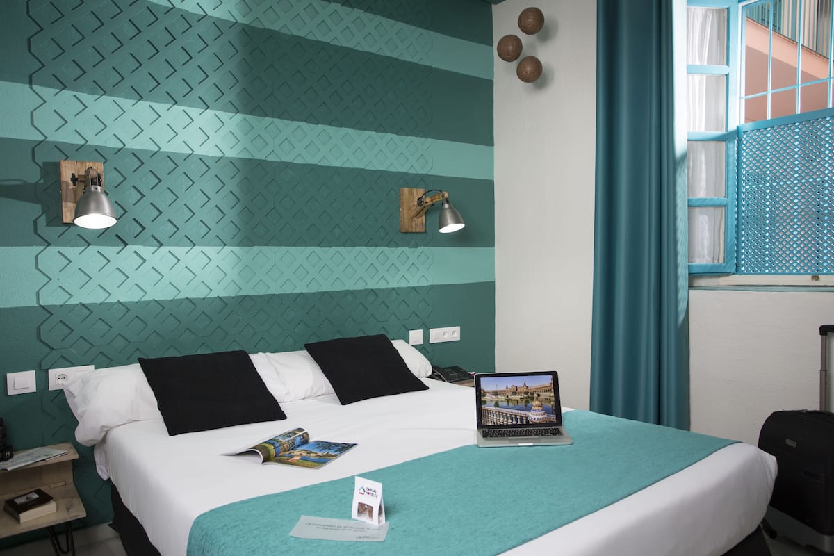 Una habitación de hotel con una cama, una computadora portátil, un folleto y una ventana con cortinas.