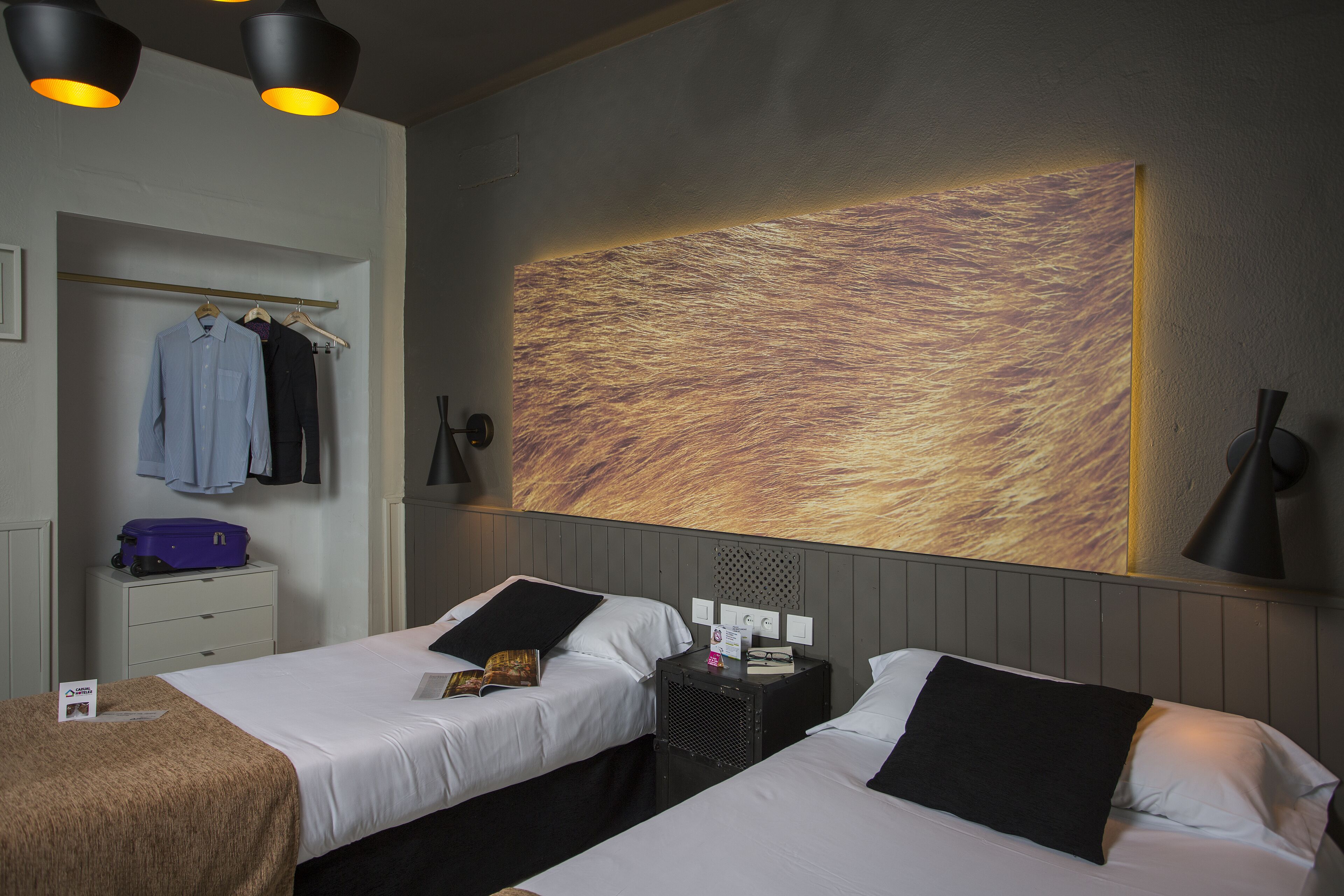 Habitación de hotel con dos camas, un armario, una mesita de noche y una obra de arte colgada en la pared.