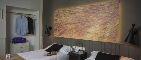 Habitación de hotel con dos camas, un armario, una mesita de noche y una obra de arte colgada en la pared.