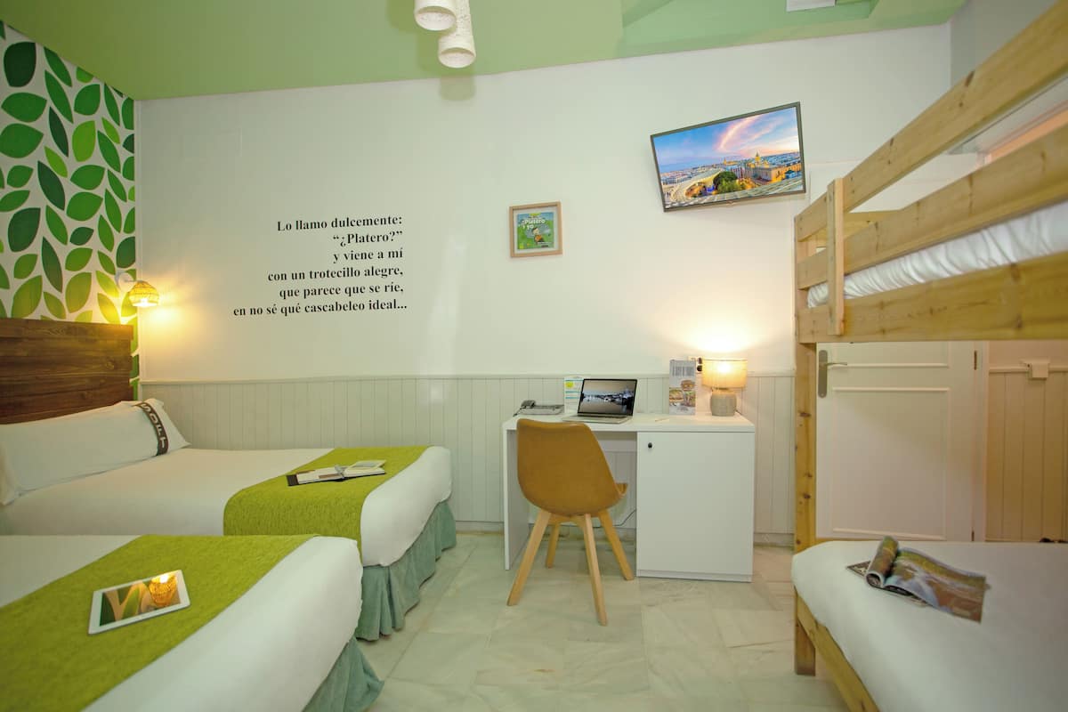 Habitación de hotel con dos camas, un escritorio, una silla, un refrigerador pequeño y una pared decorada con una cita y una fotografía.