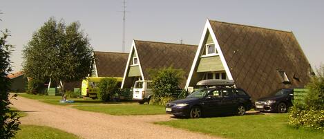 A row of A-frame cottages with a gravel driveway, parked cars, and a clear sky.
