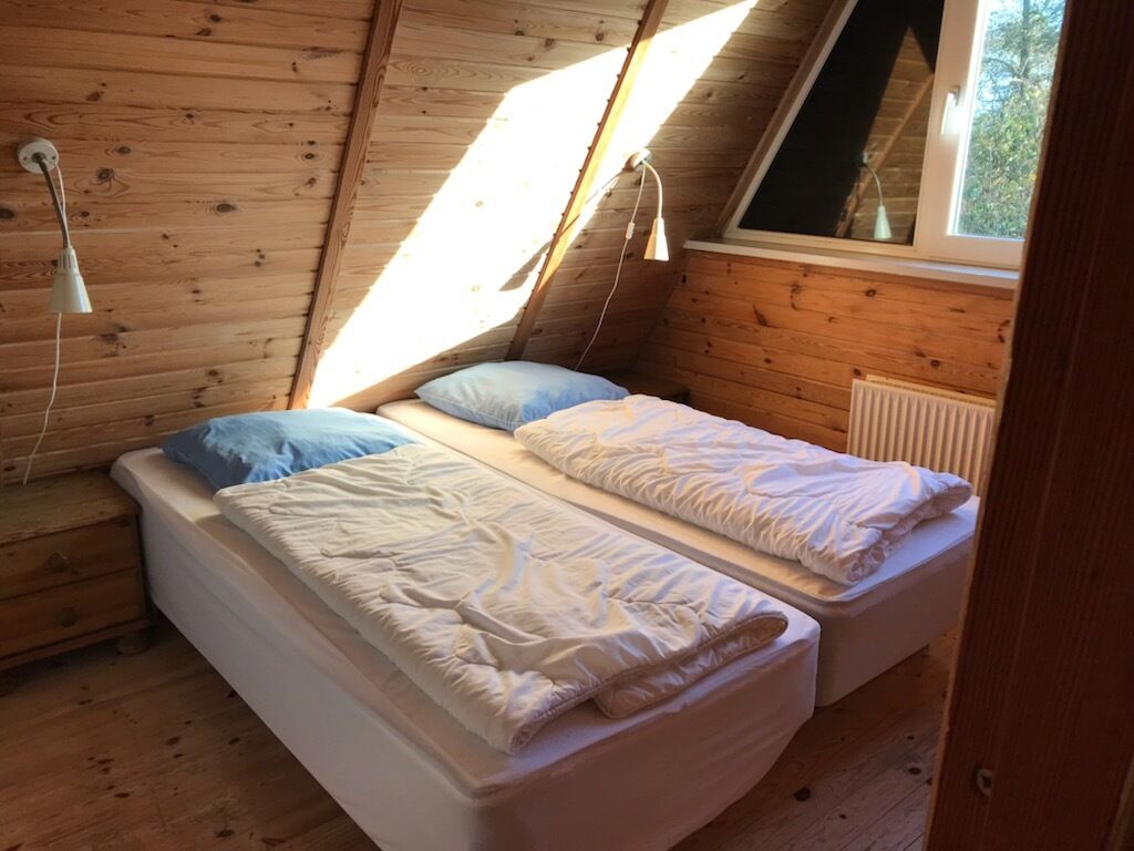 A small, wooden-paneled room with two beds, a window, and a radiator.