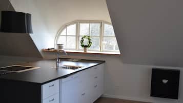 Een moderne keuken met een zwart aanrecht, witte kastjes, een roestvrijstalen spoelbak en een raam met een krans.