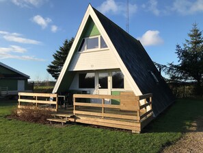 A triangular A-frame building with a wooden deck and a green door.