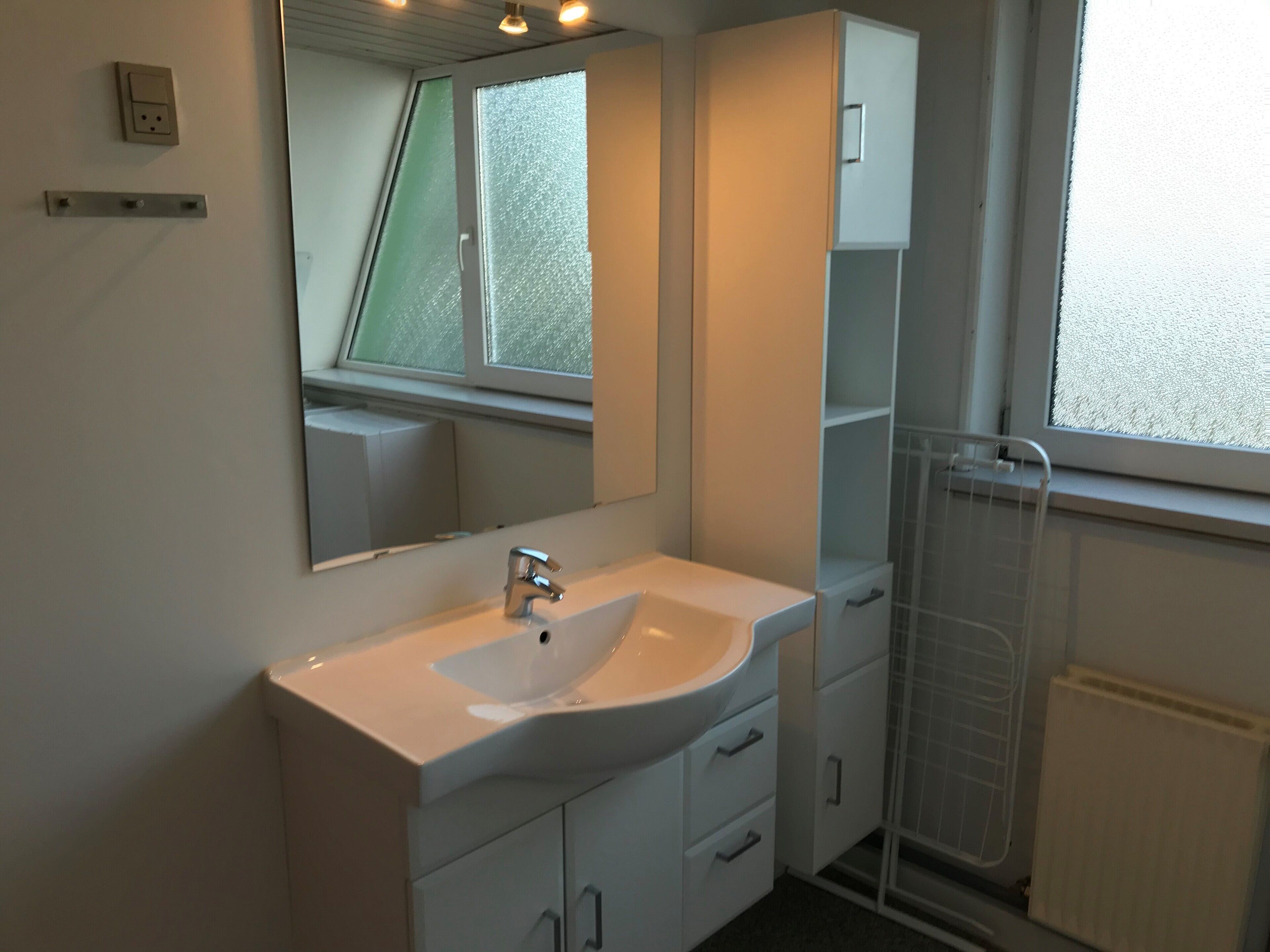Un baño moderno con un lavamanos blanco, un espejo y una ventana.