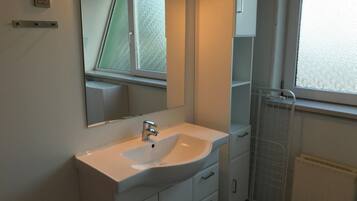 Un baño moderno con un lavamanos blanco, un espejo y una ventana.