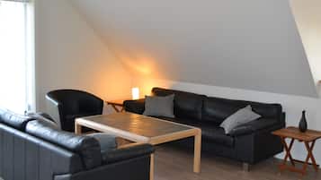 A modern living room with a black leather sofa, a wooden coffee table, and a small wooden side table.