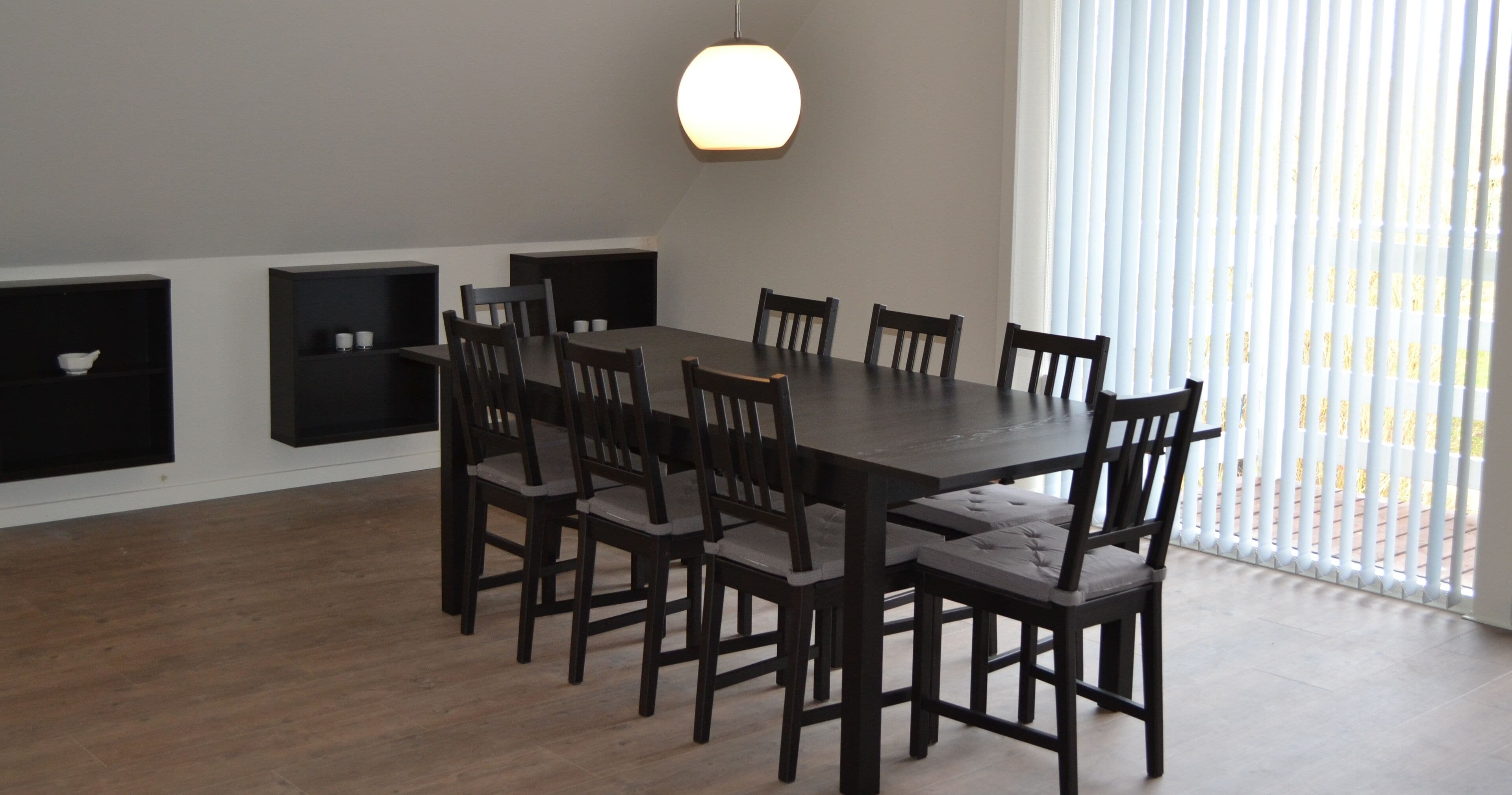 Un comedor con una amplia mesa rectangular rodeada de sillas, una lámpara colgante y estanterías empotradas en la pared.