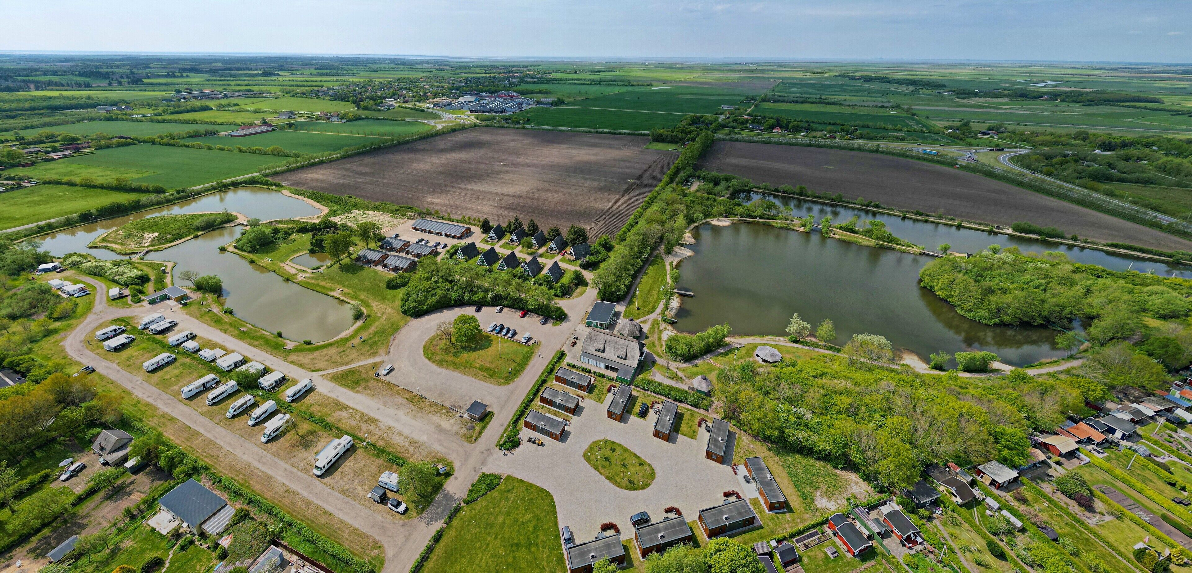 Oversigtsbillede af et landligt område med en stor mark, flere søer og en parkeringsplads med autocampere.