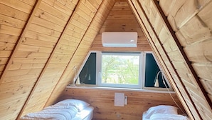 A small, cozy attic bedroom with two single beds, wooden walls, a window with a view of greenery, and an air conditioning unit. - Storkesøen Ribe (Ribe)