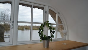 A window with a view of a lake, a potted plant, and a wine glass on a wooden ledge. - Storkesøen Ribe (Ribe)