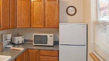 Una cocina con armarios de madera, microondas, tostadora, refrigerador y un reloj en la pared.