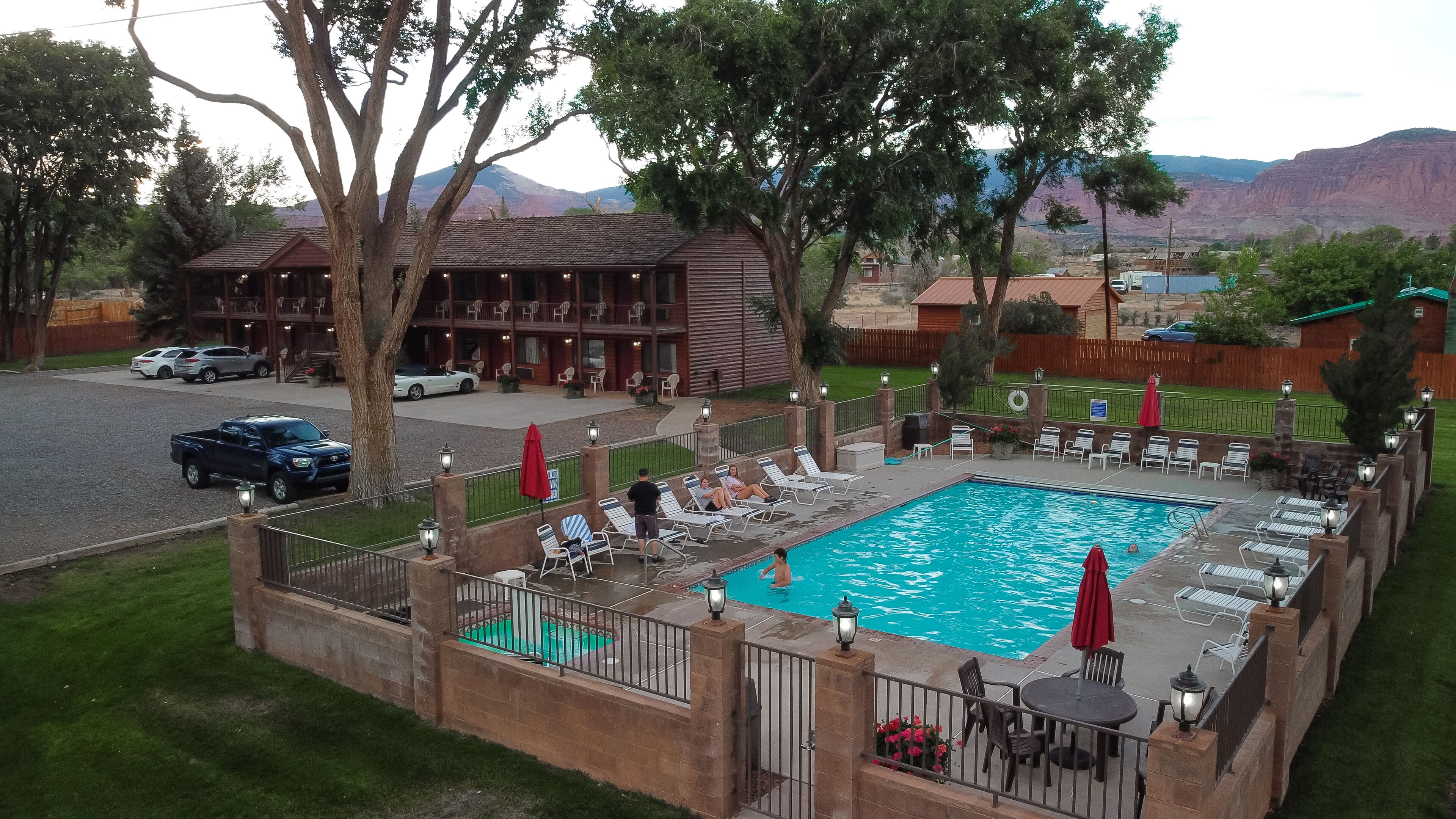 A pool area with lounge chairs and umbrellas, a wooden building with a balcony, and a mountainous backdrop.