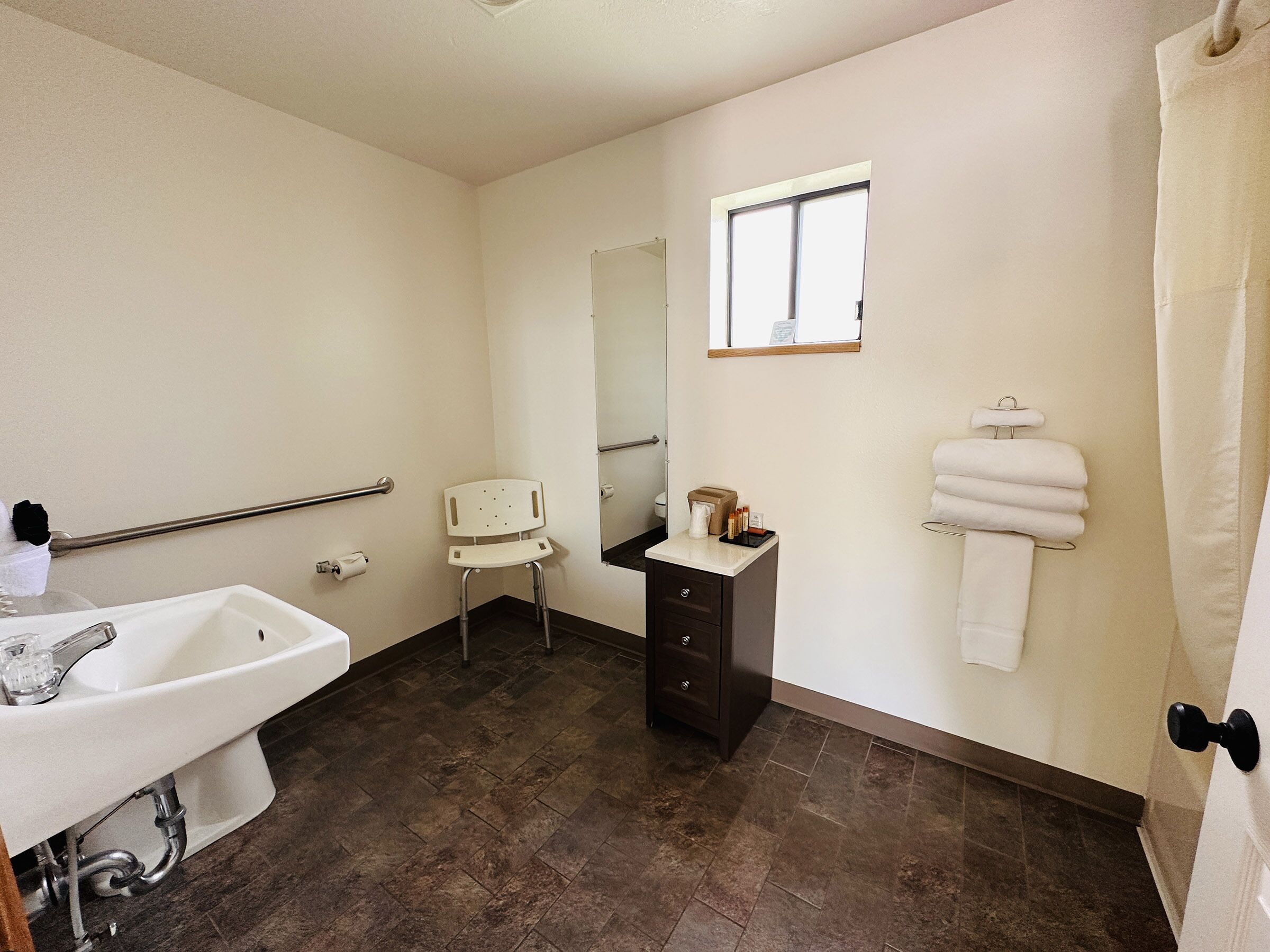 Un baño con lavamanos blanco, un espejo, una ventana, un perchero y una silla.