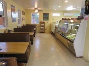 Un restaurante con cabinas y una barra. Hay cuadros en las paredes, un ventilador de techo y una ventana con vistas a árboles.
