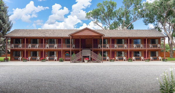 Un motel de estilo cabaña de madera de dos pisos, con un porche central, varios balcones y mobiliario exterior.