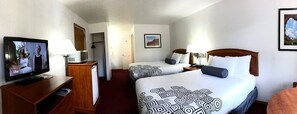Habitación de hotel con dos camas, un televisor, un escritorio y una puerta que da a un pasillo.