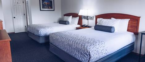Een hotelkamer met twee bedden, een deur, een ingelijst kunstwerk aan de muur en een nachtkastje met een lamp.