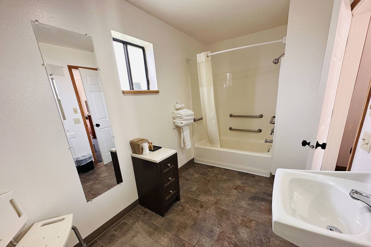 A bathroom with a bathtub, a sink, a mirror, and a window.