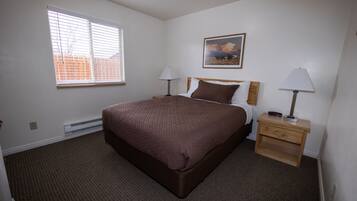 A bedroom with a bed, two bedside tables with lamps, a heater, a window, and a painting on the wall.