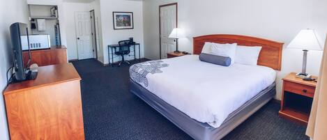 A hotel room with a bed, two bedside tables with lamps, a desk with a chair, a television, and a painting on the wall.