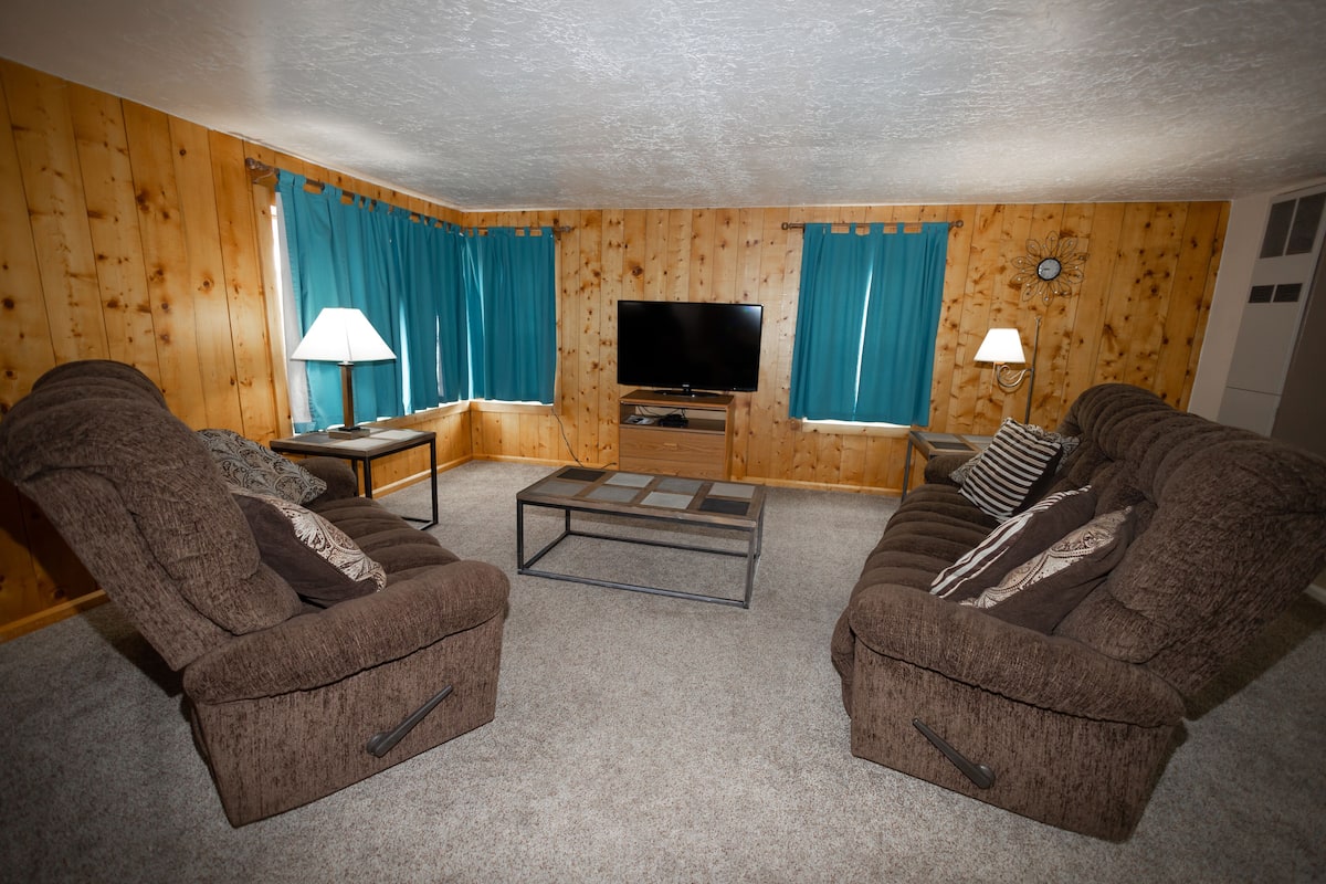 A living room with two brown armchairs, a coffee table, a flat-screen TV, and a lamp on a side table.