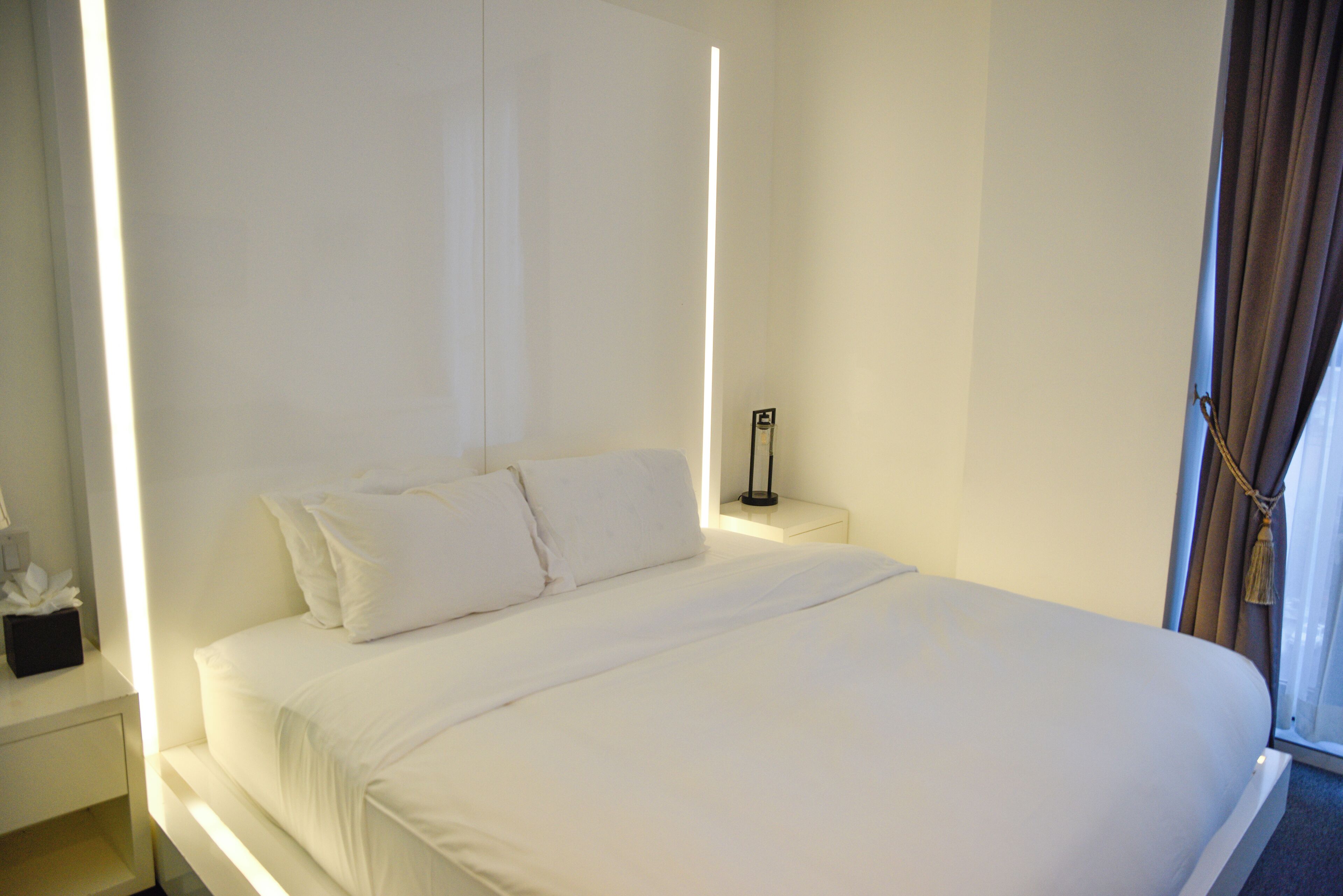 A neatly made bed in a hotel room with a bedside table and a lamp.