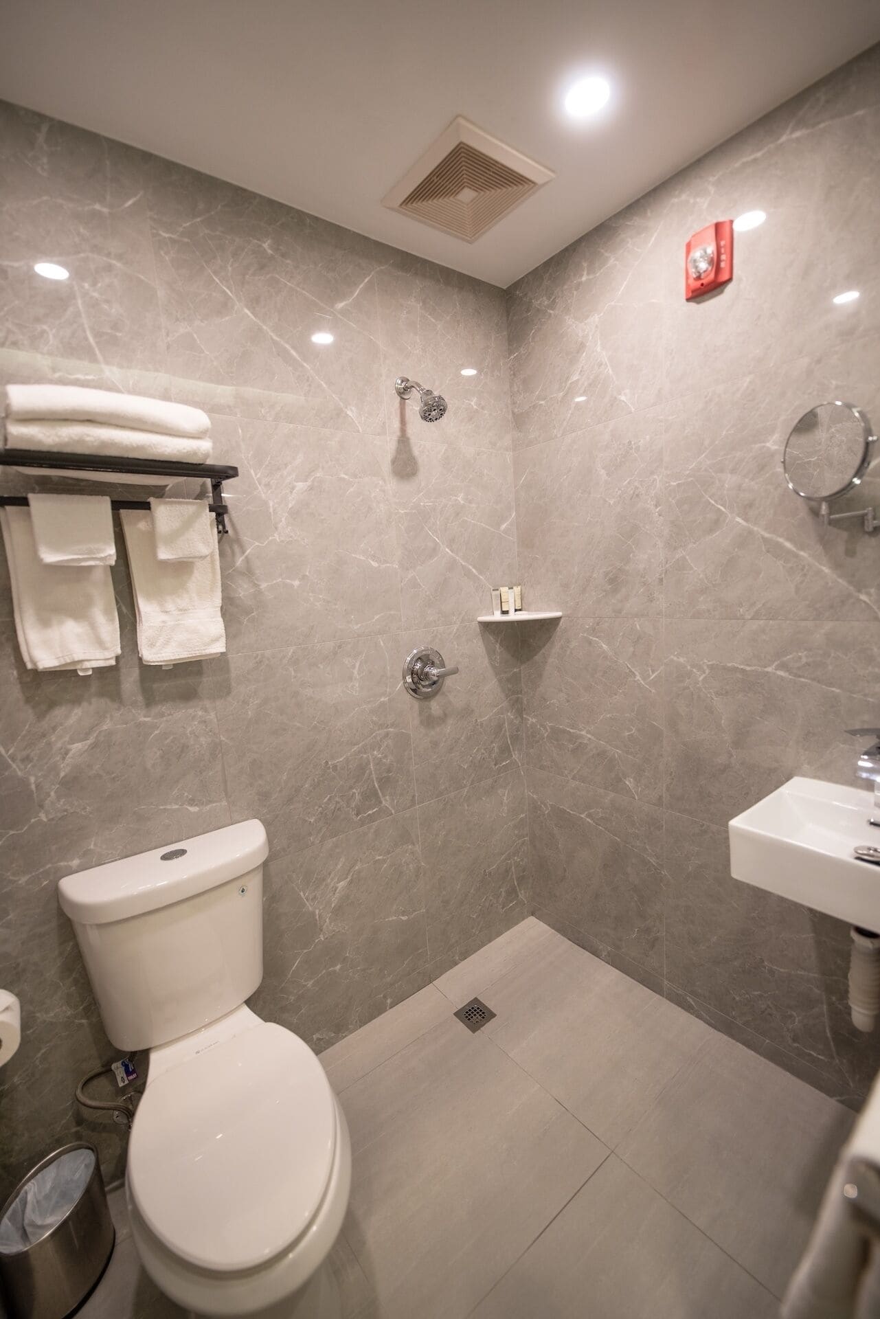 Et moderne badeværelse med toilet, bruser og håndvask, marmorvægge og et håndklædestativ.