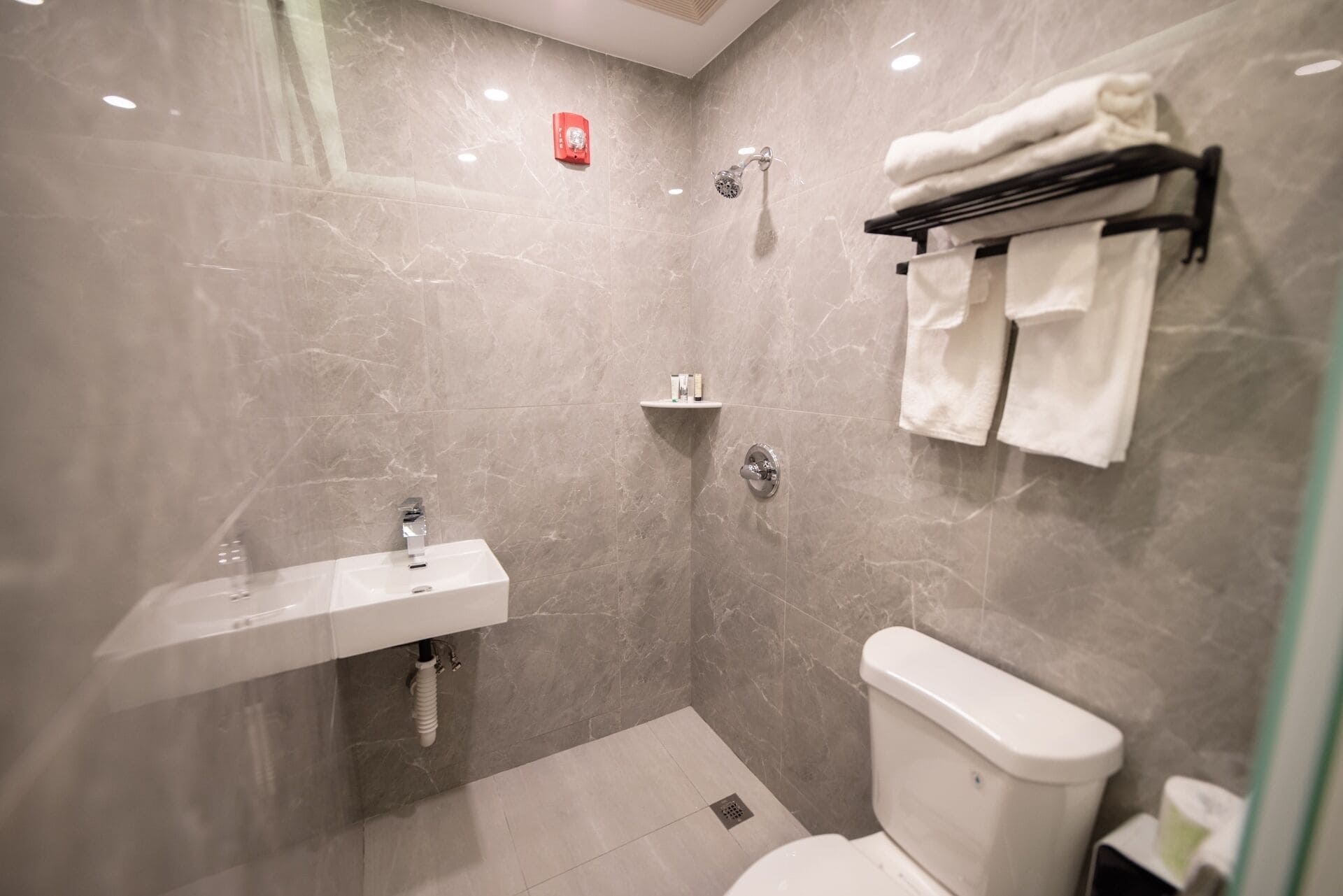 A modern bathroom with a marble wall, a white sink, a toilet, a shower, and a towel rack.