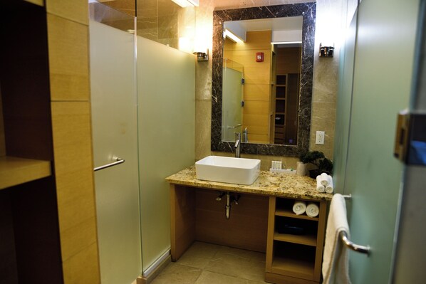 Une salle de bain avec une douche à parois de verre, un lavabo blanc et un plan de toilette en marbre.