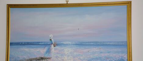 A painting of a woman in a white dress standing by the sea with a golden frame.
