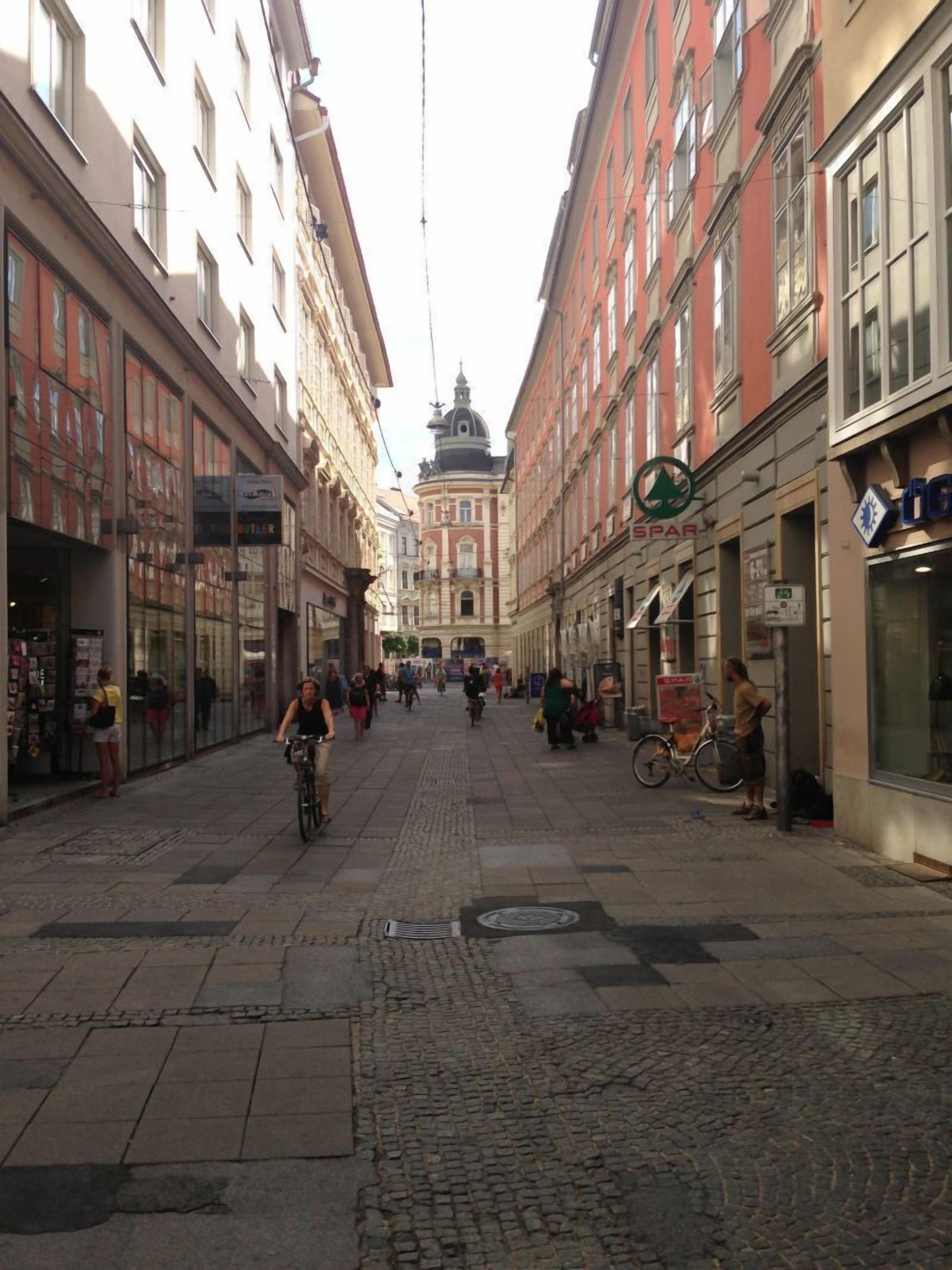 A cobblestone street lined with historic buildings, a cyclist, and pedestrians.