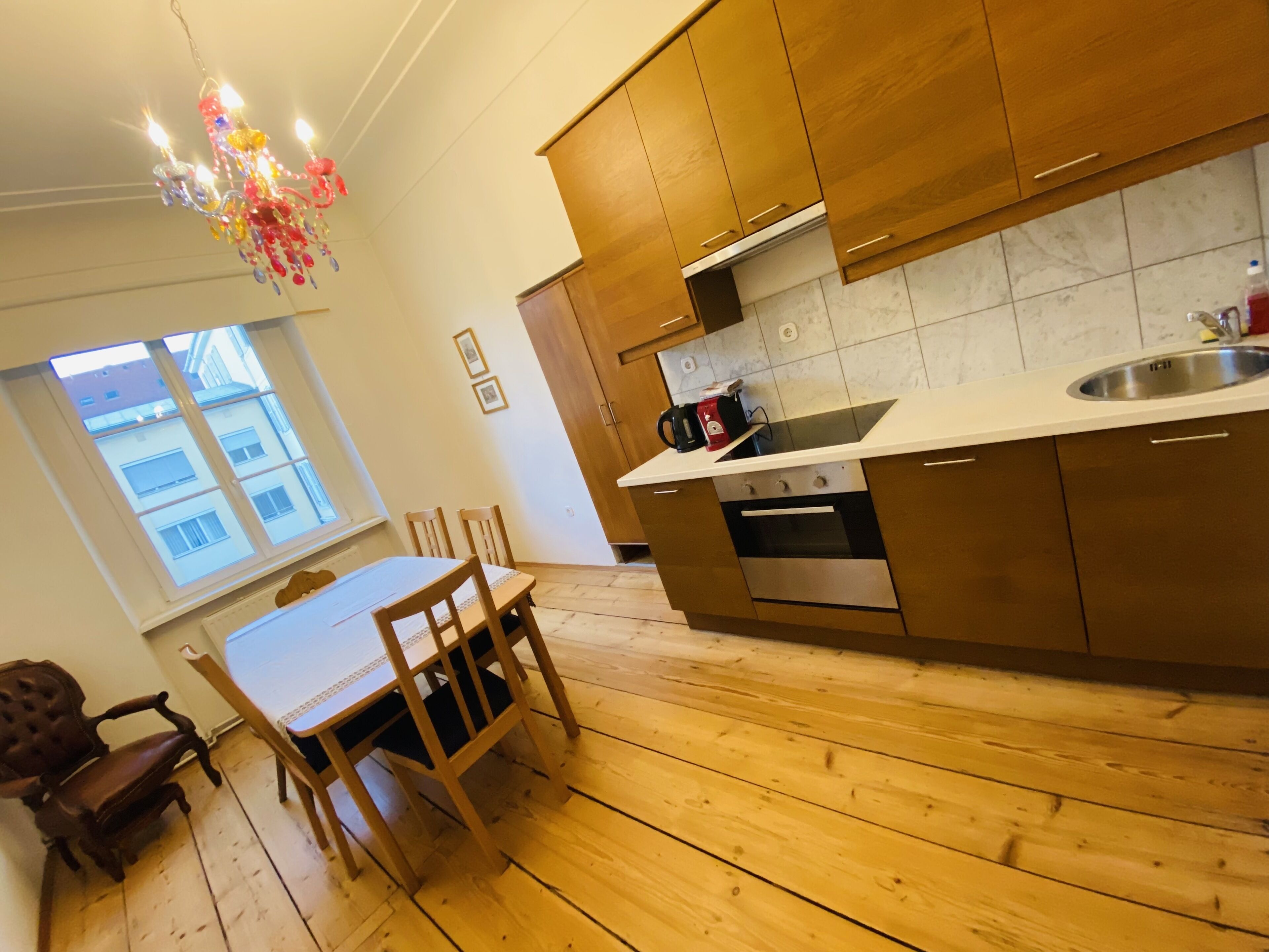 A modern kitchen with wooden cabinets, a stainless steel sink, and a dining area with a table and chairs.