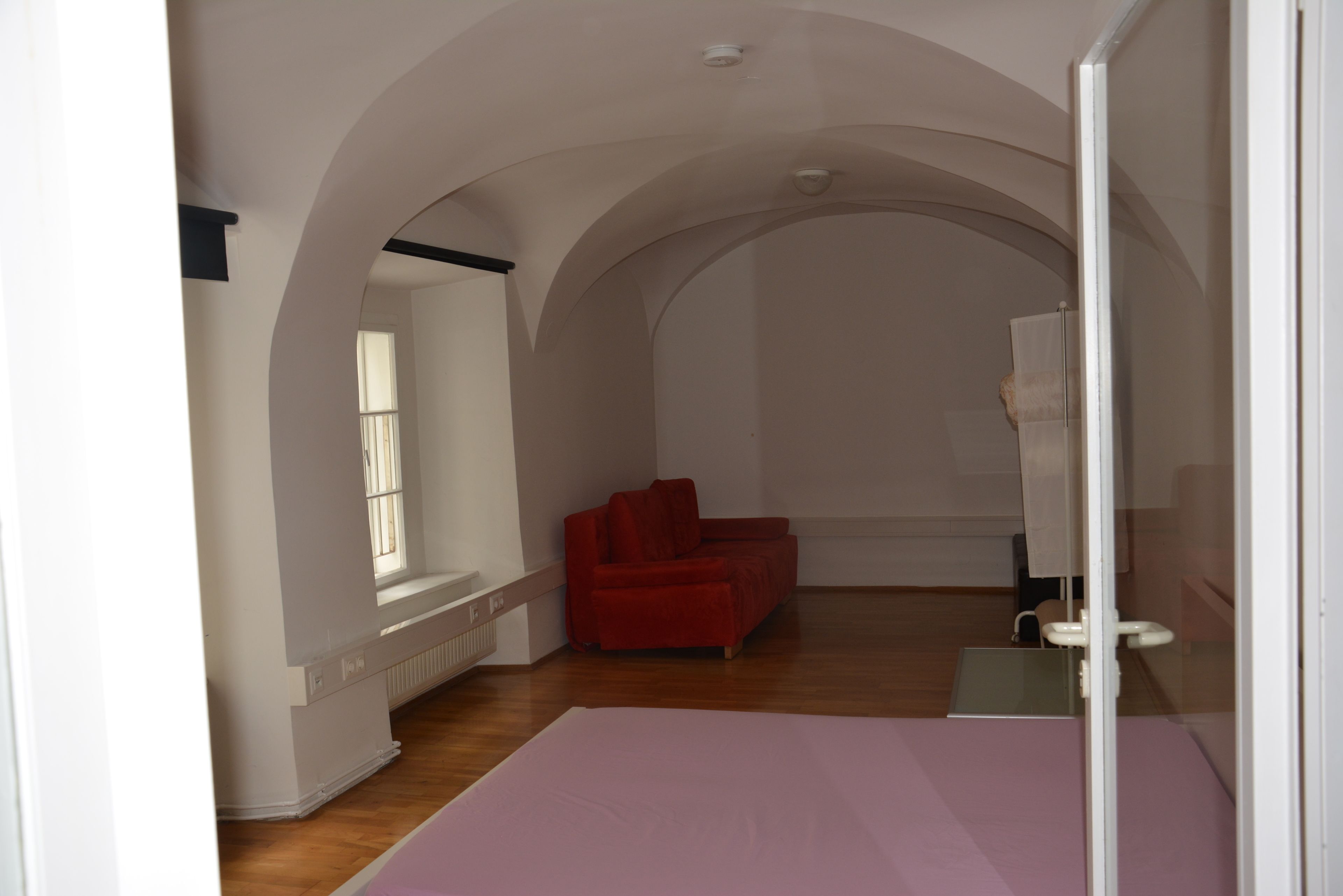 A room with a red sofa, a white radiator, and a window with blinds.