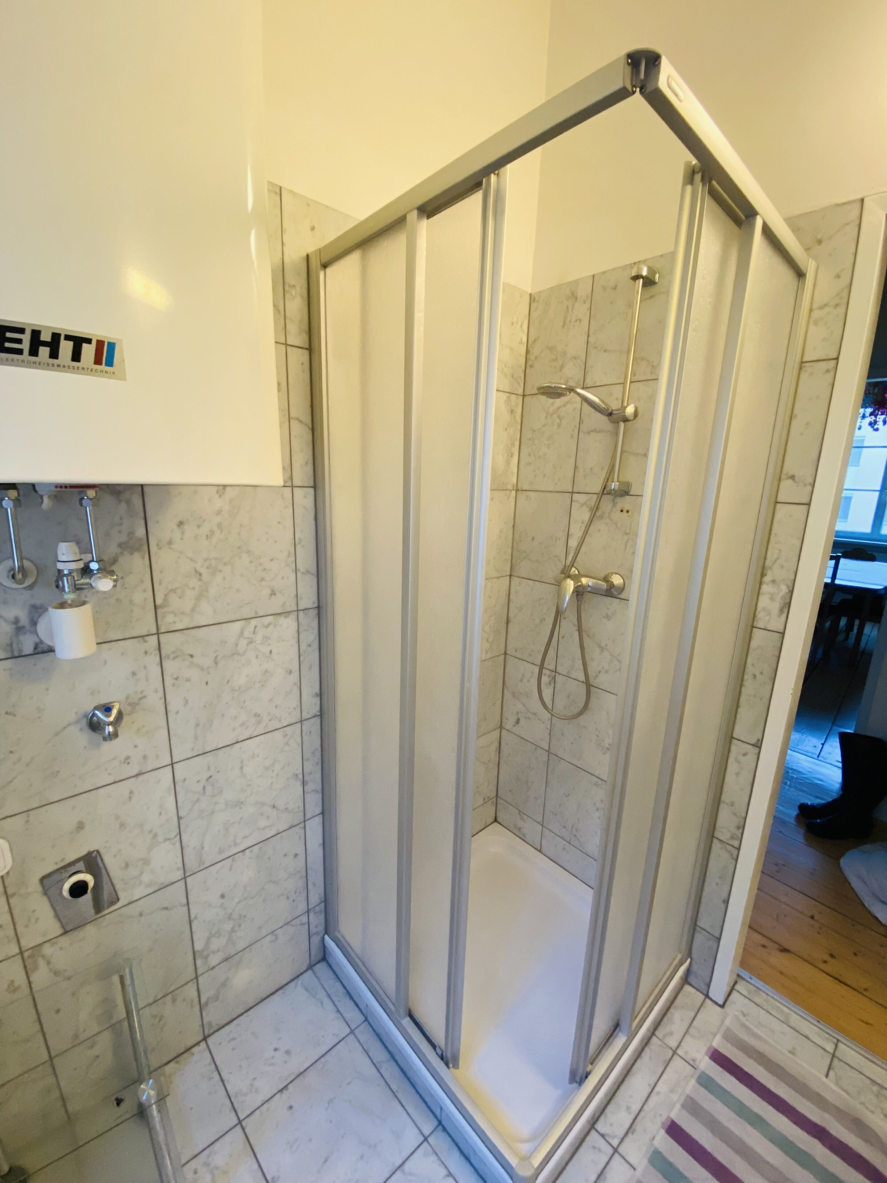 Une salle de bain moderne avec une douche à parois de verre, des murs carrelés et un porte-rouleau de papier toilette visible.