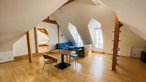 A spacious attic room with wooden beams, a loft bed, a blue sofa, and a dining table. - Hans-Sachs-Gasse 10 (Graz)