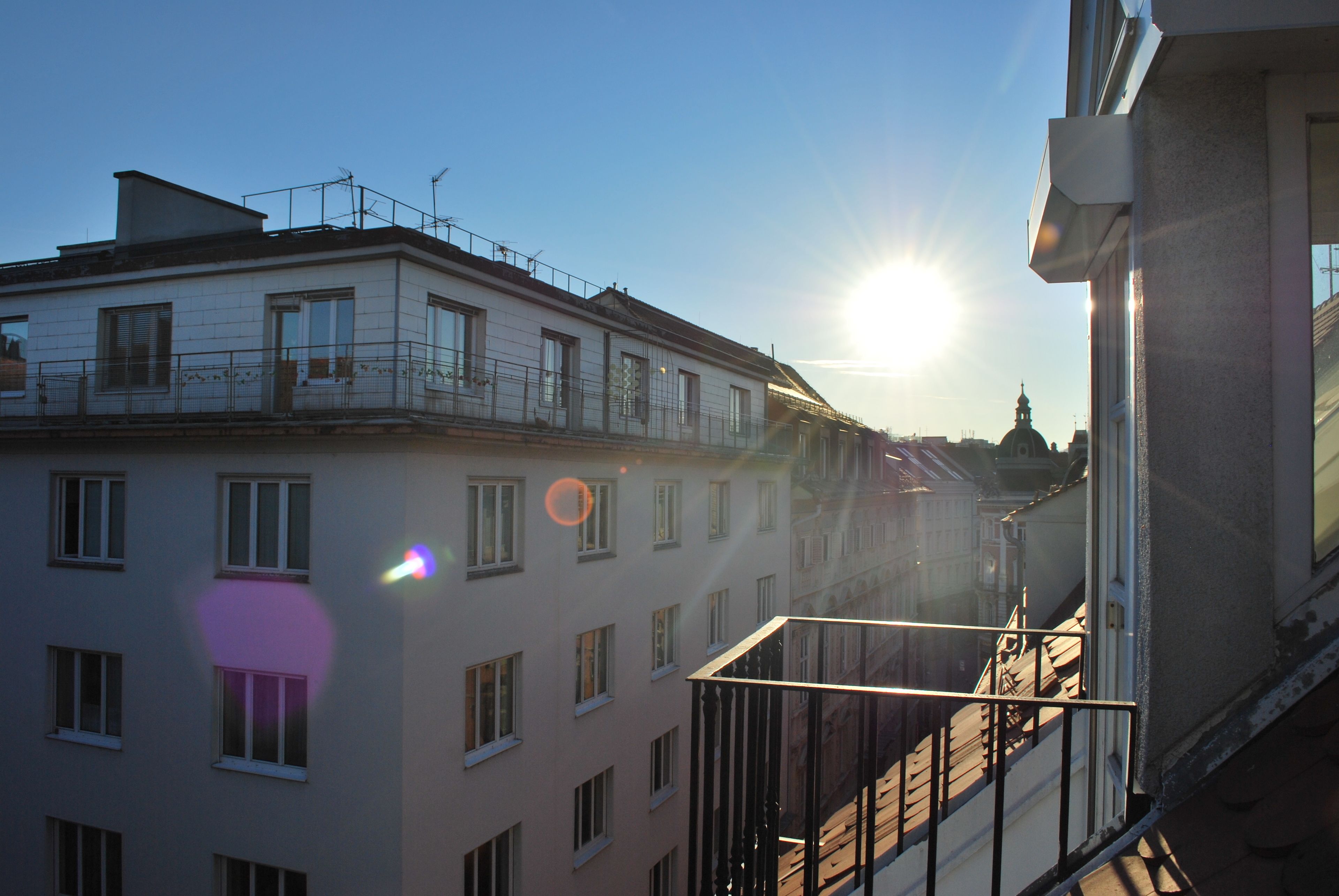 A building with multiple windows and balconies, a clear sky, and the sun shining.