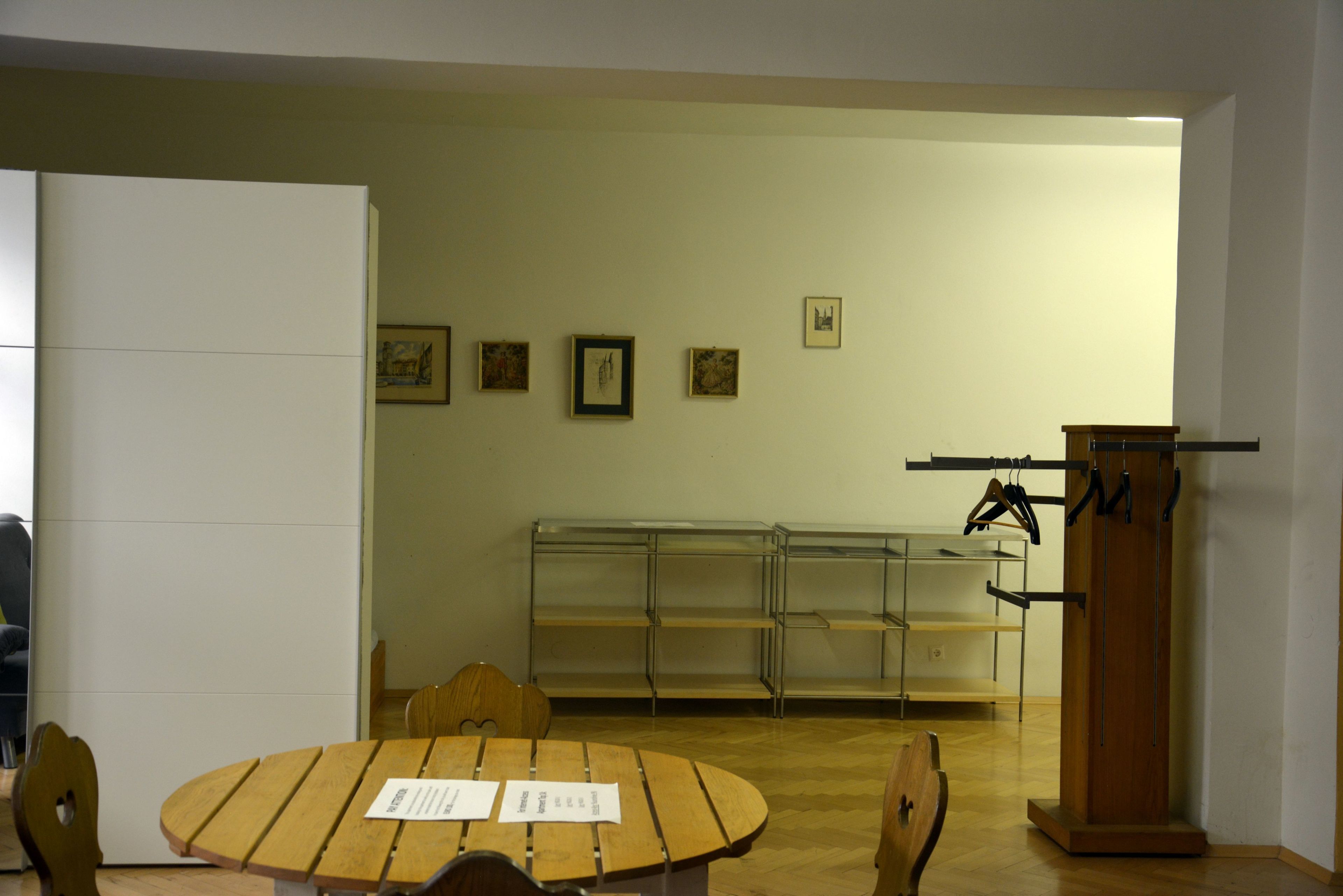 A room with a round wooden table, chairs, a podium, and a wall with framed pictures.