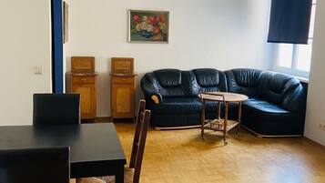 Una sala moderna con un sofá de cuero negro, una mesa de comedor con sillas, una pequeña mesita auxiliar de madera y un colgador de luz.