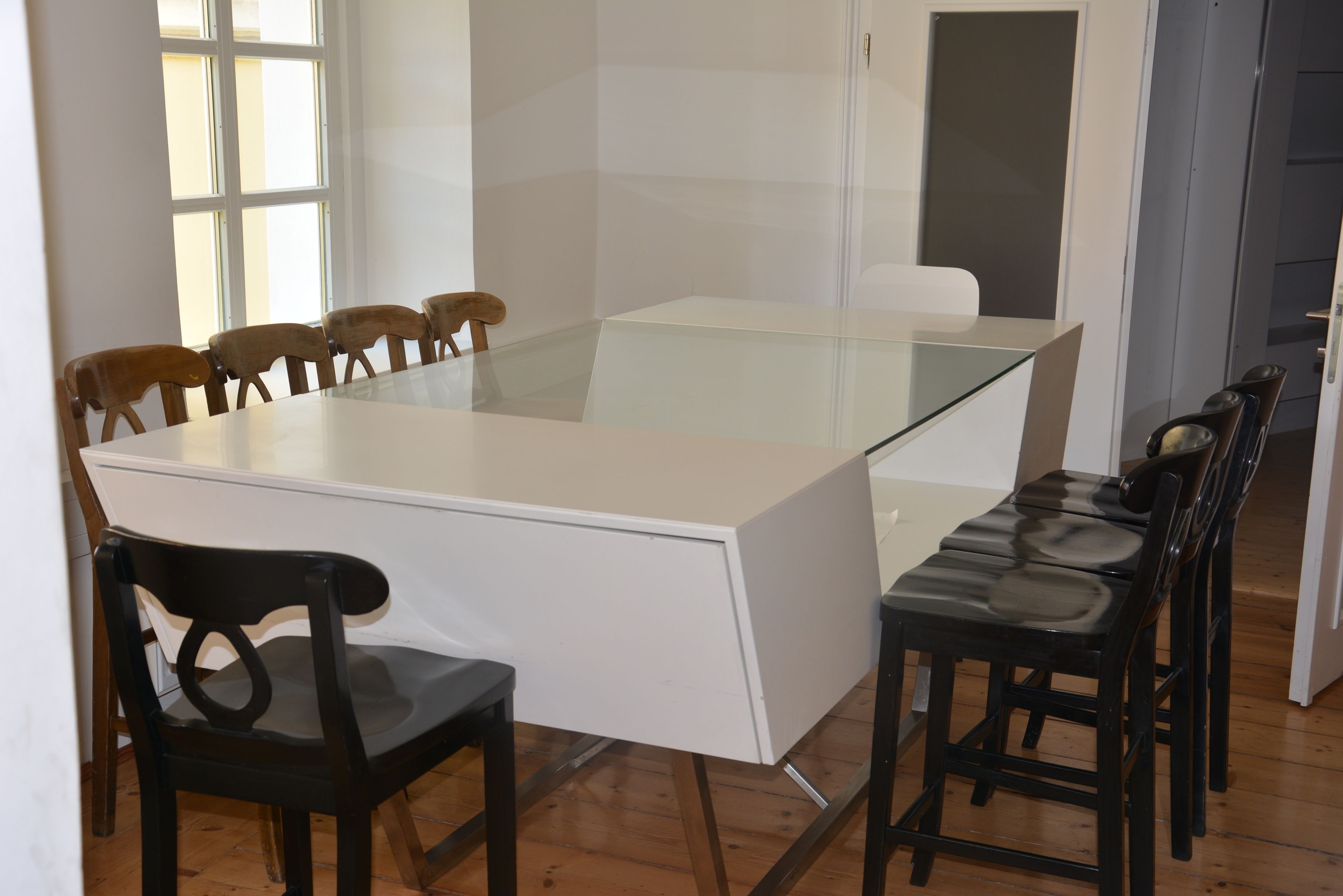 Un espace repas moderne avec une table à plateau en verre, des chaises en bois et un meuble blanc.