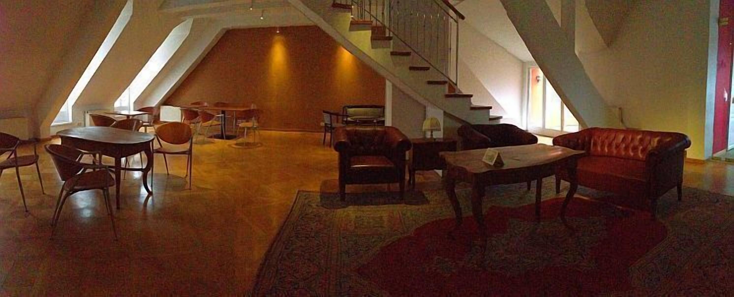 A spacious loft with a high ceiling, a staircase, and a mix of seating areas including a sofa and chairs.