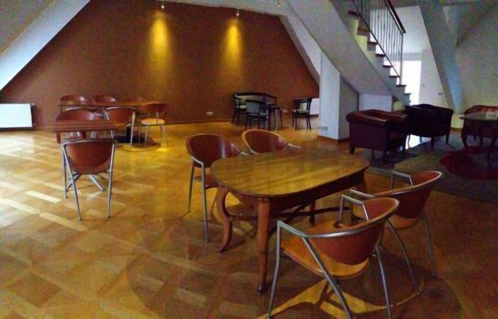 A spacious room with a large wooden table and chairs, a staircase, and a high ceiling.