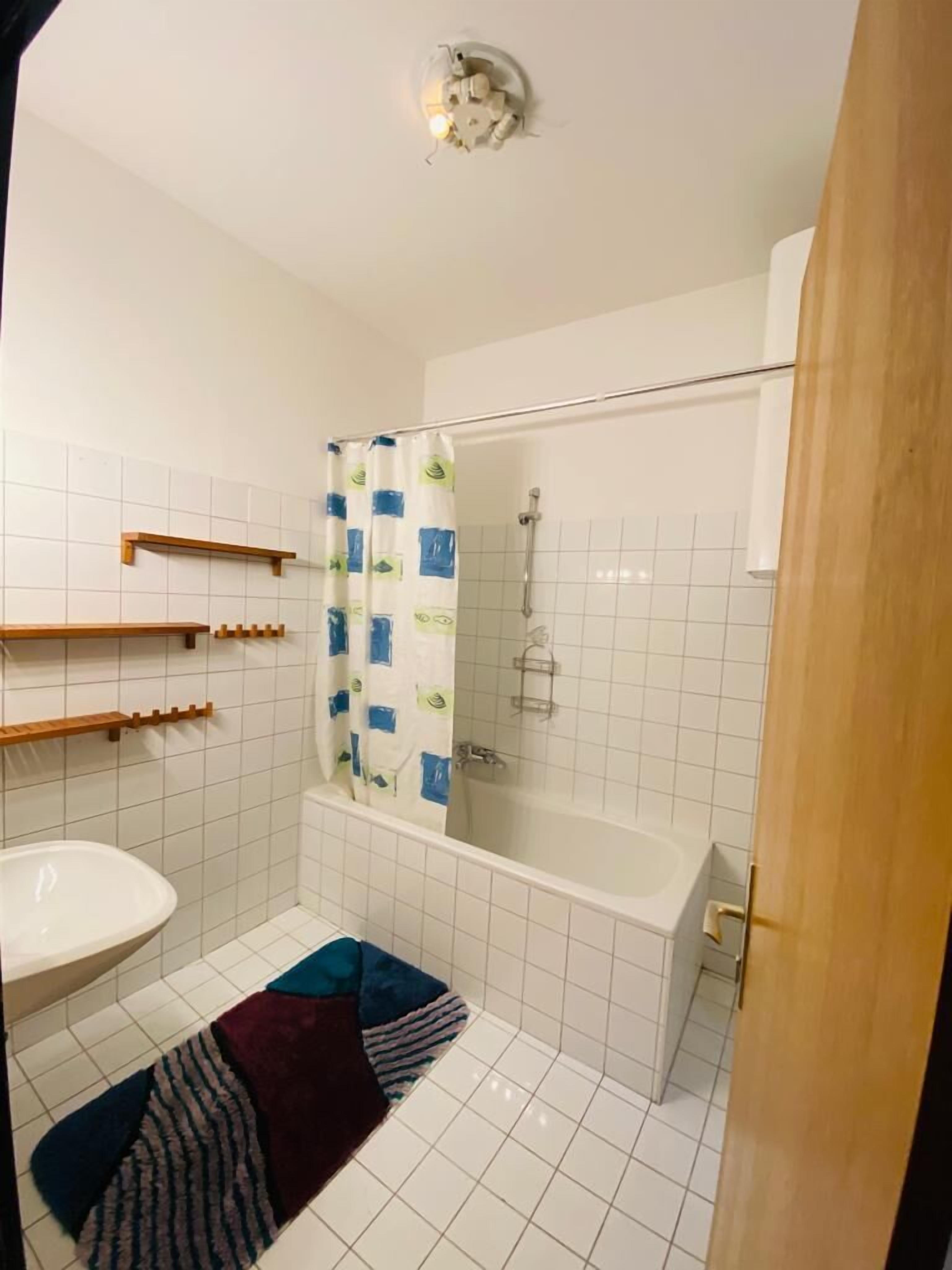 A bathroom with a bathtub, a shower, a sink, and wooden shelves.