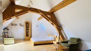 A loft bedroom with a wooden floor, a bed, a green armchair, a blue sofa, and a wooden ceiling structure. - Hans-Sachs-Gasse 10 (Graz)