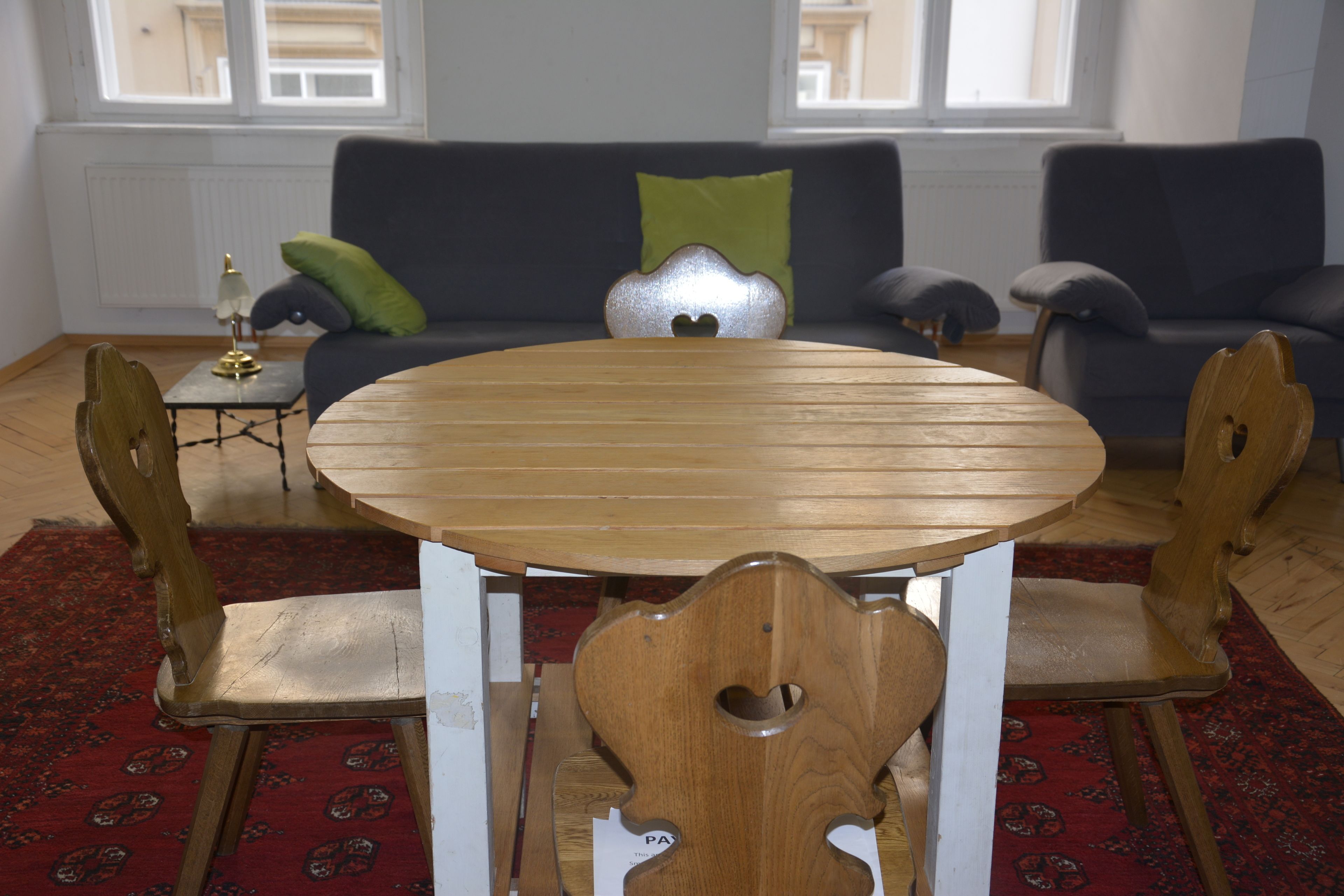 Un coin repas avec une table ronde en bois, quatre chaises, une petite table d’appoint avec une lampe, et un canapé avec des coussins en arrière-plan.