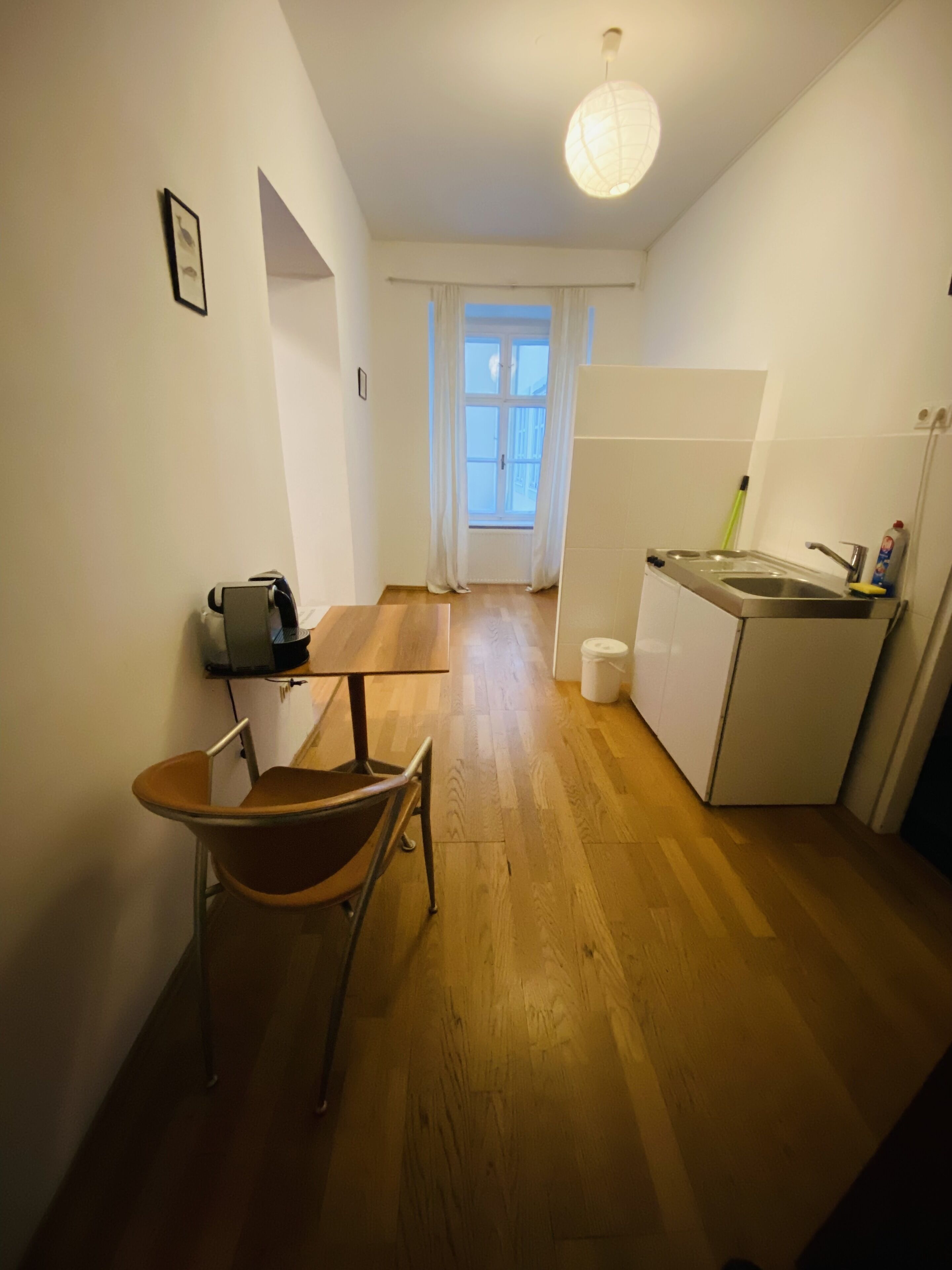 Eine kleine Küche mit Esstisch und Stuhl, einem Kühlschrank und einem Fenster mit Vorhängen.