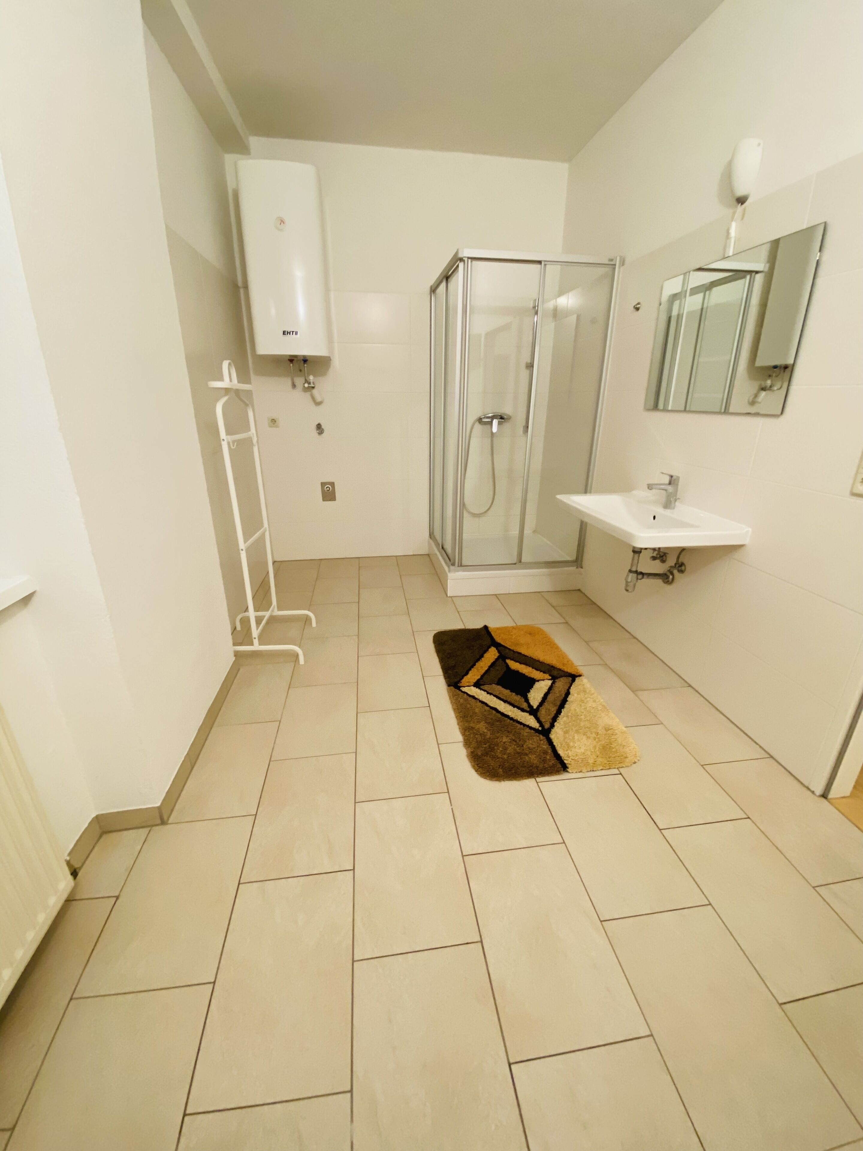 A bathroom with a shower, sink, and towel rack.